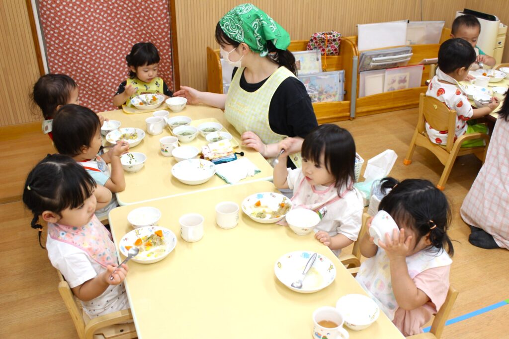 自園調理の給食を保育士に見守られながら食べる園児たち