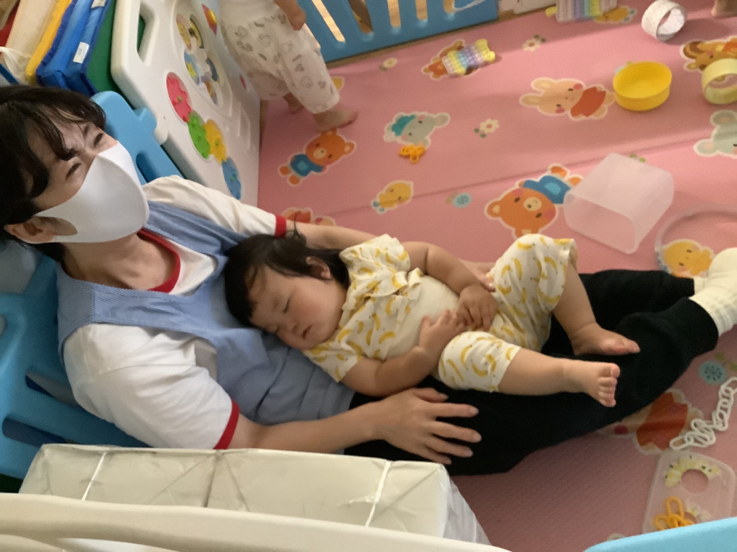 くじら保育園 三国園で、午睡で保育士の膝の上で寝る園児