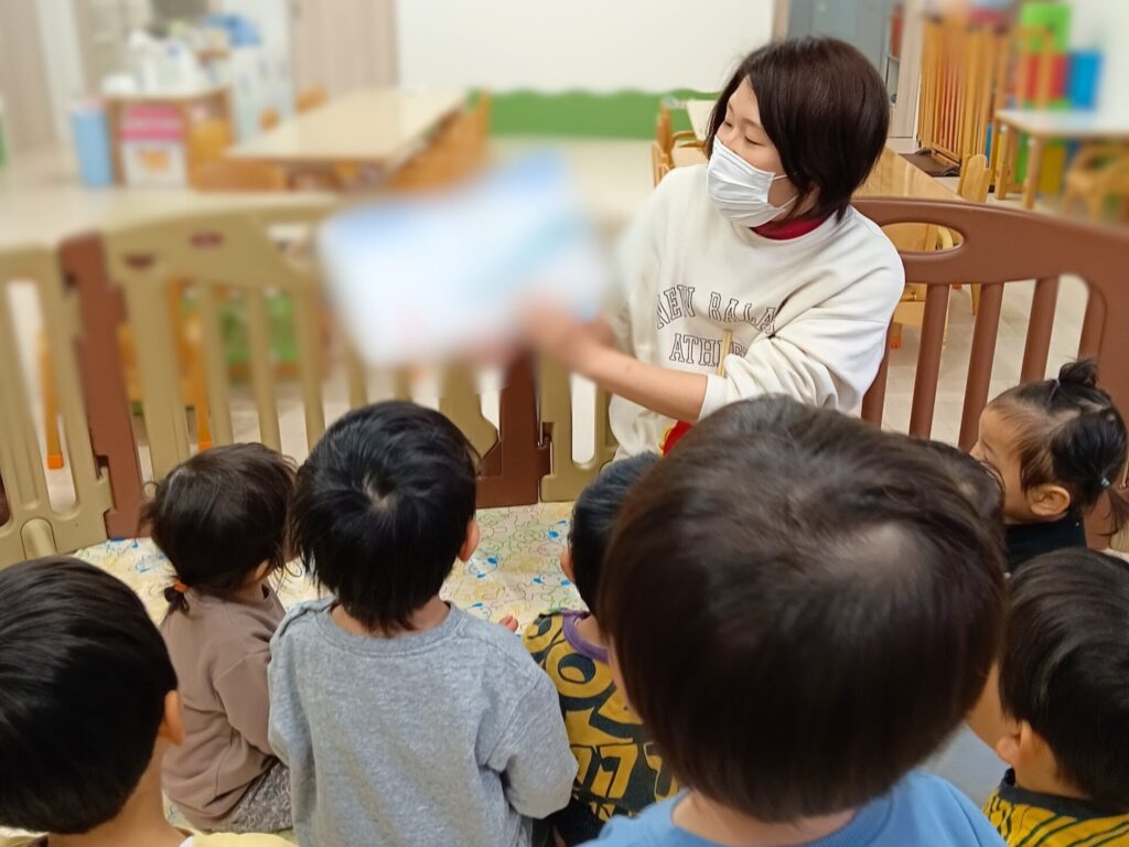 おおぞら保育園 西新町園で、絵本を読んでもらう園児